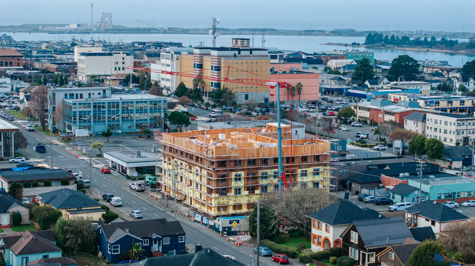 Construction-progress drone aerial of a mid-rise build with tower crane over downtown
