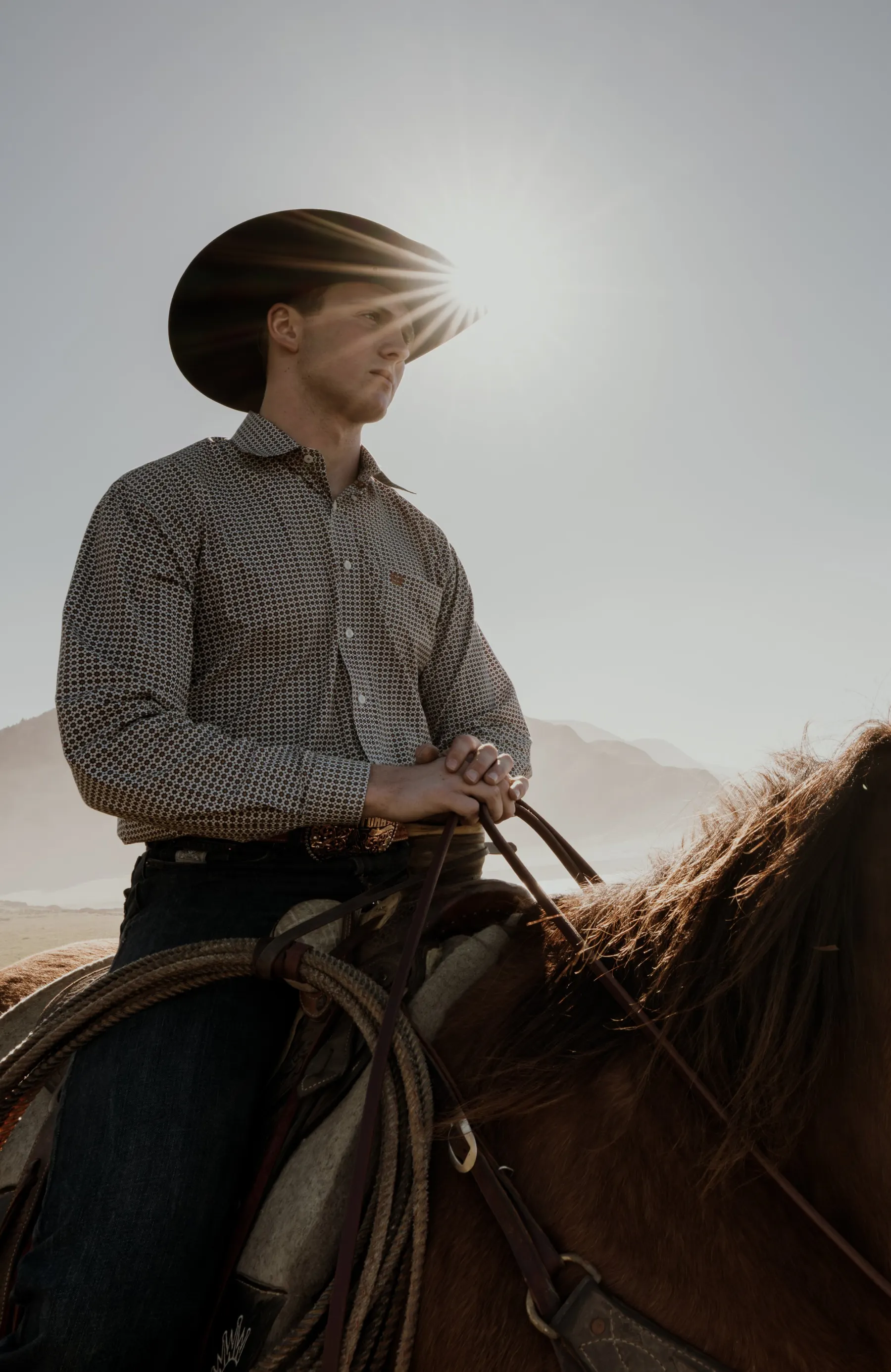 Senior portrait on horseback with cowboy hat and sun flare, ranch-country senior session