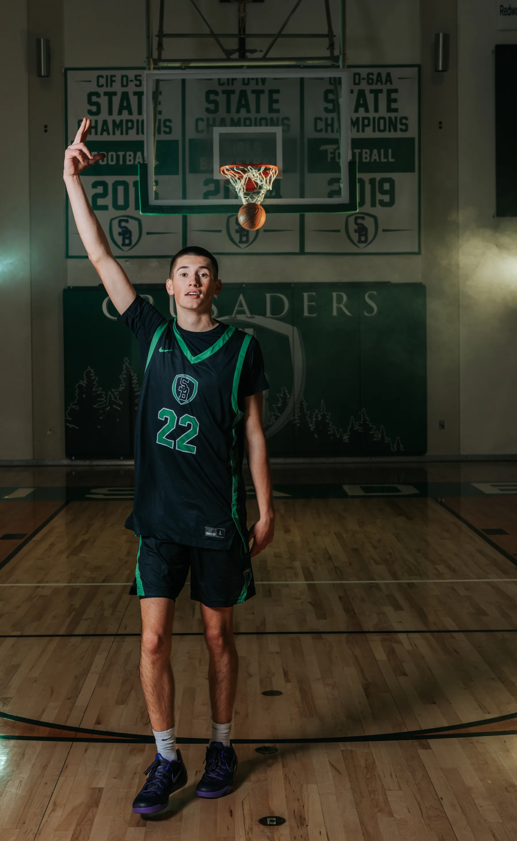 Basketball player posed beneath the hoop and state-championship banners, flash-lit