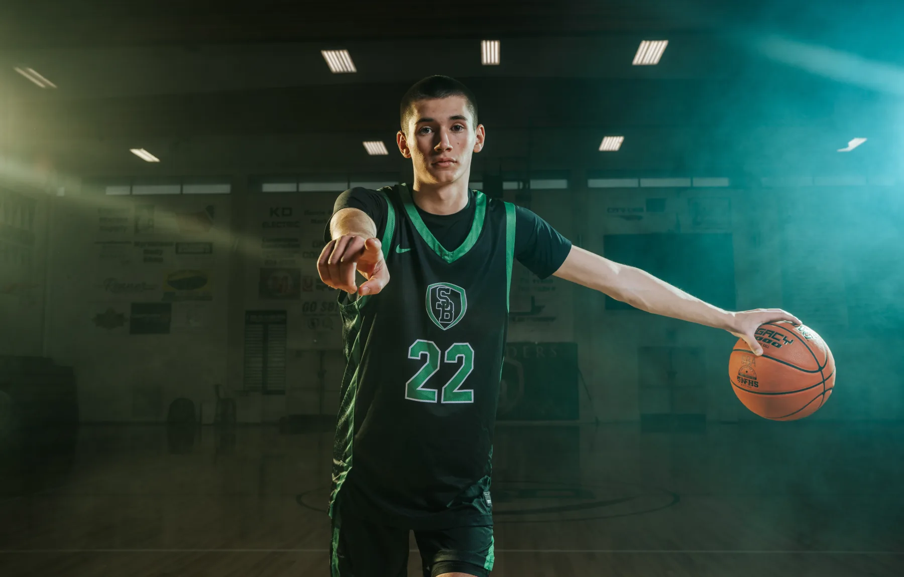 Basketball player pointing down the lens, strobe-lit gym fog behind